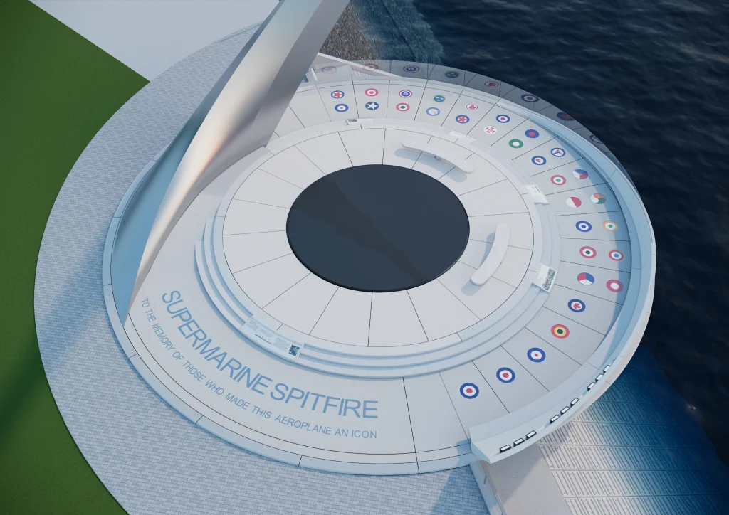 Aerial view of a circular memorial plaza by the water, featuring labelled plaques with colourful air force roundels, white seating, and the inscription “SUPERMARINE SPITFIRE honouring the aircraft and its makers.
