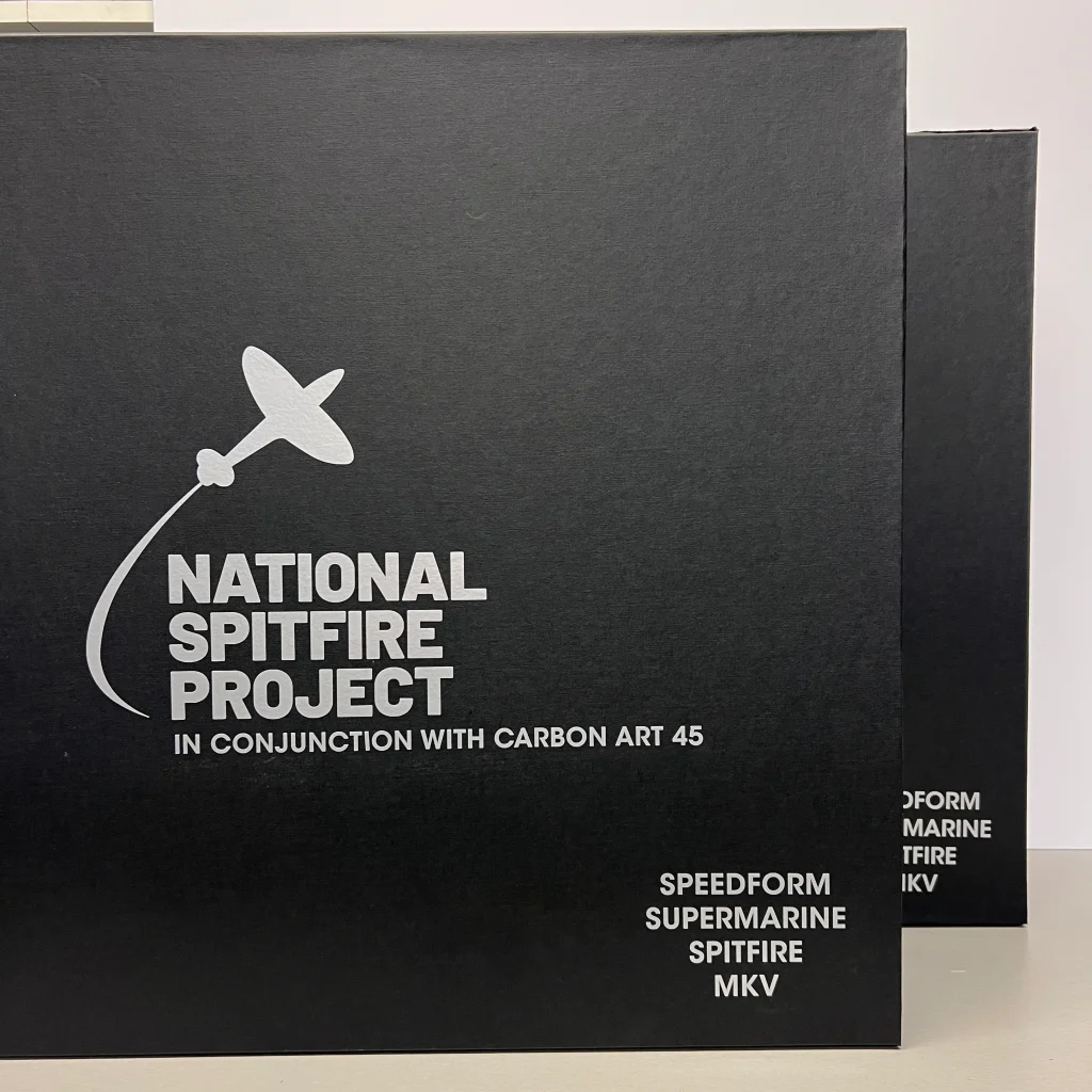 Black boxes with white text and a silhouette of a Spitfire aeroplane. Text reads: National Spitfire Project in conjunction with Carbon Art 45 and Speedform Supermarine Spitfire MKV. Another box is partially visible behind.