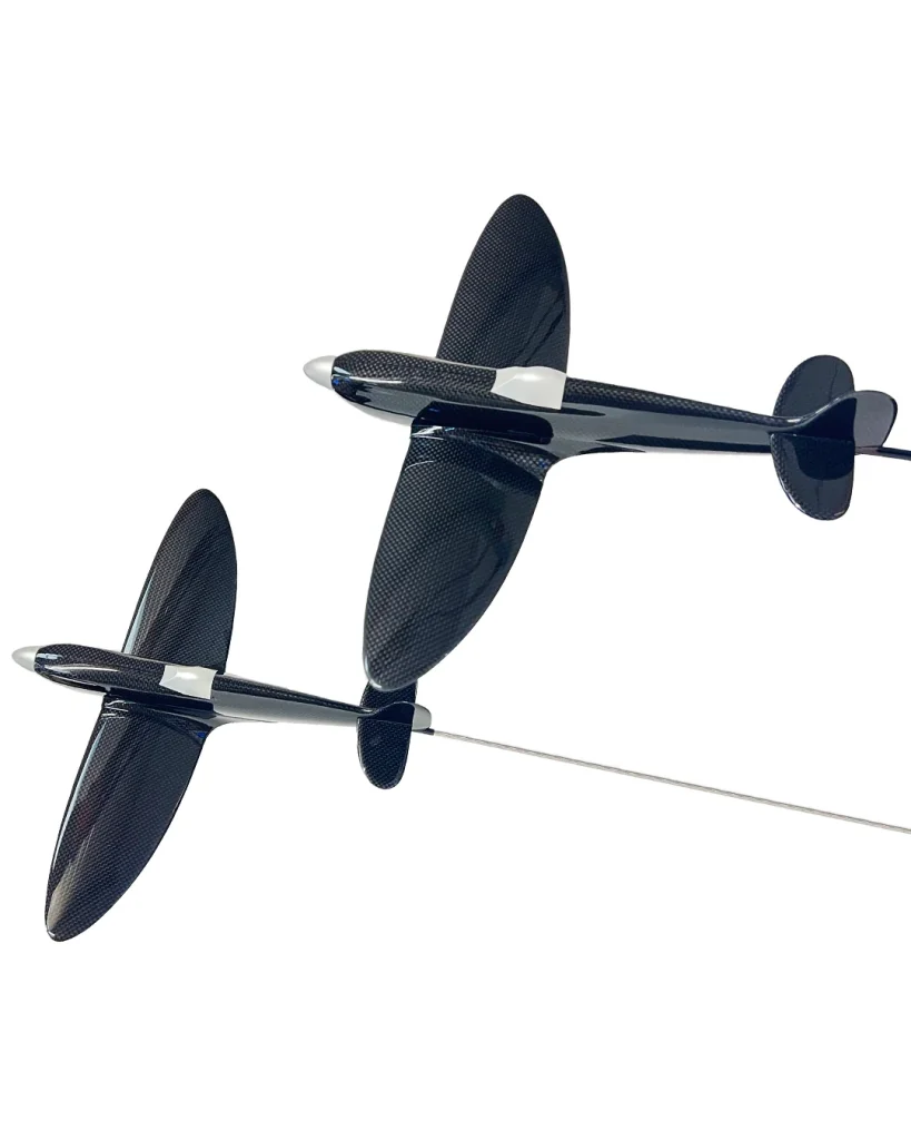 Two sleek, black carbon fibre model aeroplanes with white nose tips and tail sections are suspended by thin rods against a white background, appearing as if flying in formation.