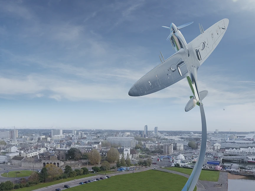 A large sculpture of a Spitfire aeroplane mounted vertically on a tall curved plinth rises above a cityscape, with buildings and a grassy area visible under a blue sky with scattered clouds.